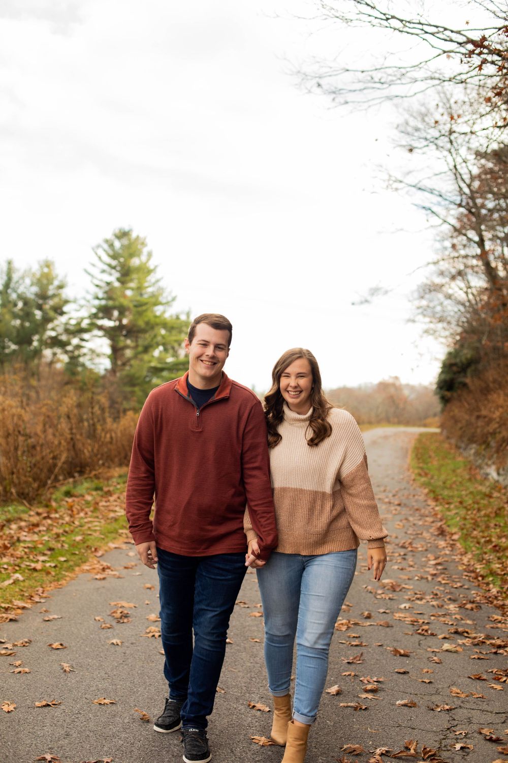 Happy couple strolling down autumn path covered in fallen leaves.