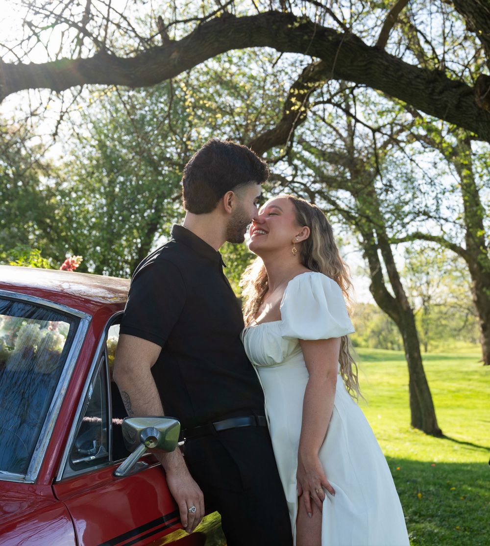 Couple shares romantic moment by vintage red car under blooming spring trees.
