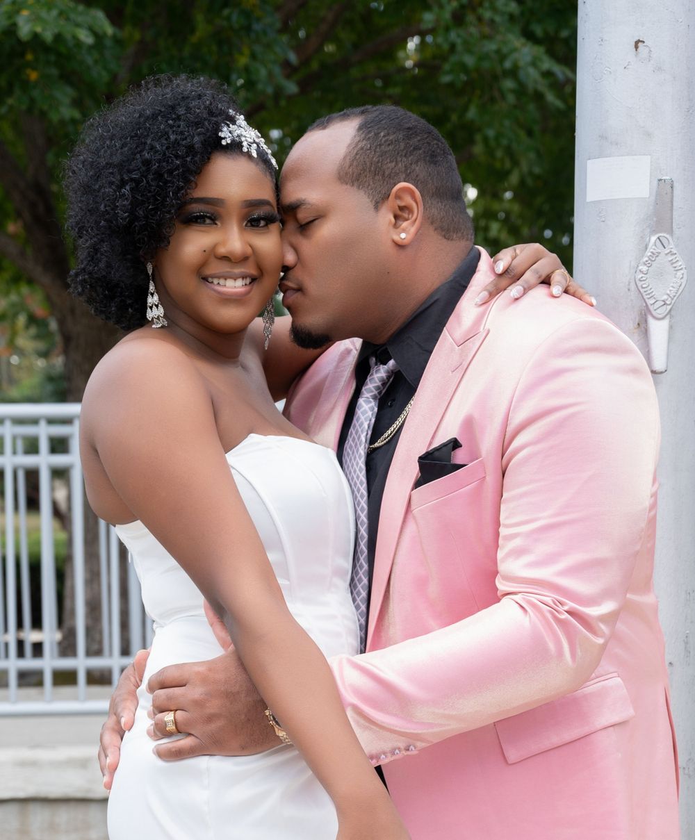 Romantic wedding couple embrace with groom in pink suit kissing bride in white dress.