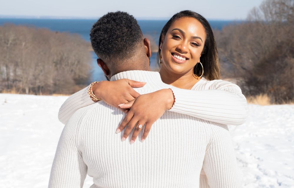 Couple in matching white sweaters embrace in snowy winter landscape.