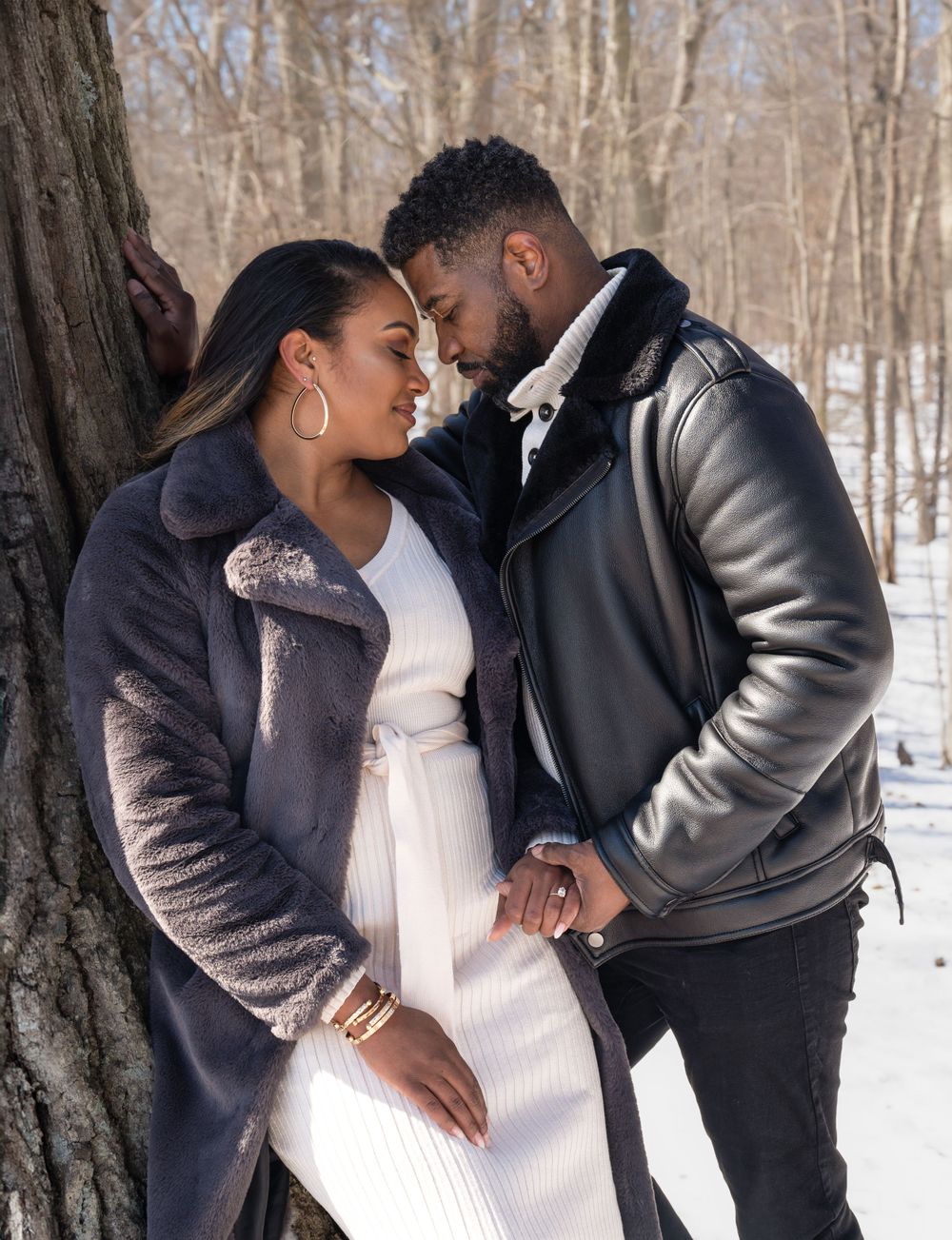Romantic couple in winter coats share intimate moment against snowy forest backdrop.