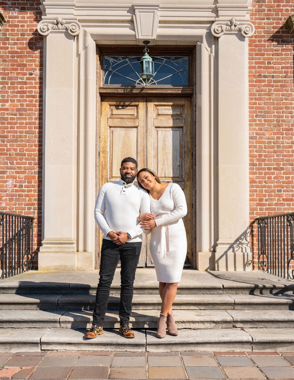 Couple poses together on steps of historic brick building with classical columns.