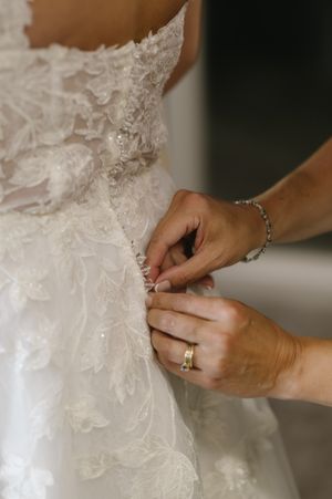 Close-up shots of hands adjusting and fastening buttons on a delicate white lace wedding dress.