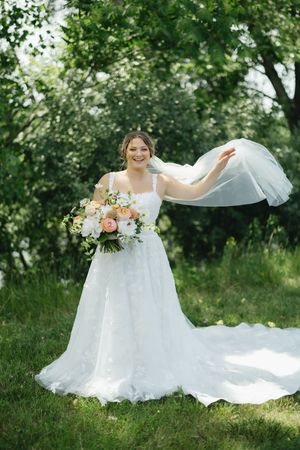 A flowing white wedding dress billows and twirls gracefully in a lush green outdoor garden setting during a summer photoshoot.