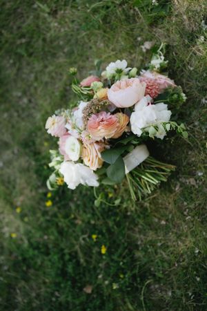 Romantic peach and blush pink floral bouquet with garden roses and greenery laying on textured surface.