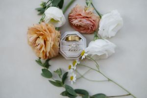 Wedding rings displayed in an octagonal ring box surrounded by peach and white roses with delicate greenery on cream surface.
