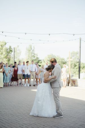 A couple shares their first dance at an outdoor wedding reception as guests watch from a distance.