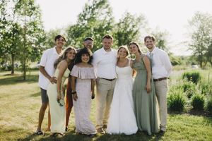 A group photo taken at a summer wedding celebration outdoors with people in white and sage green attire.