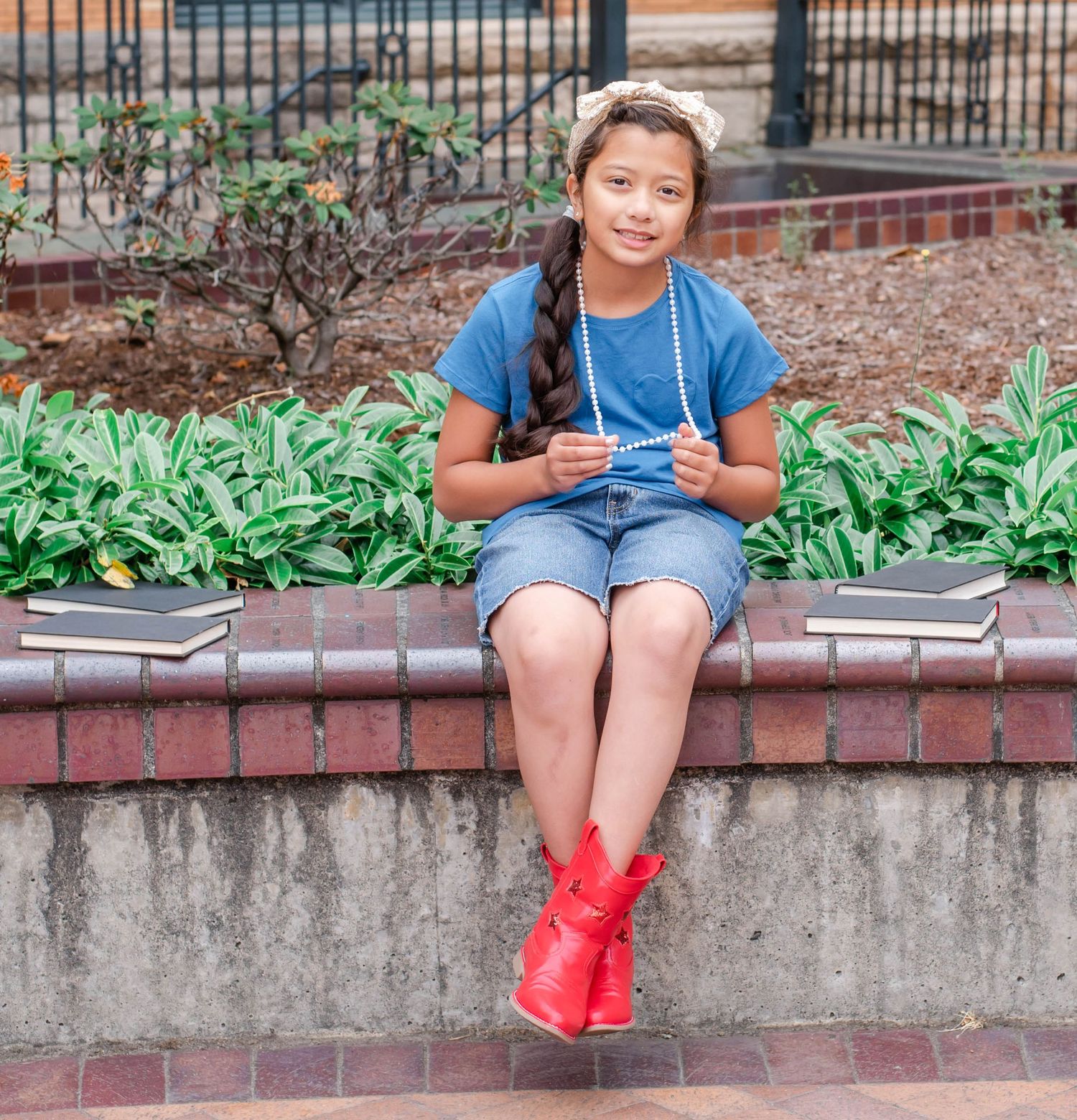 Child in red shoes sits casually on brick ledge near garden path.