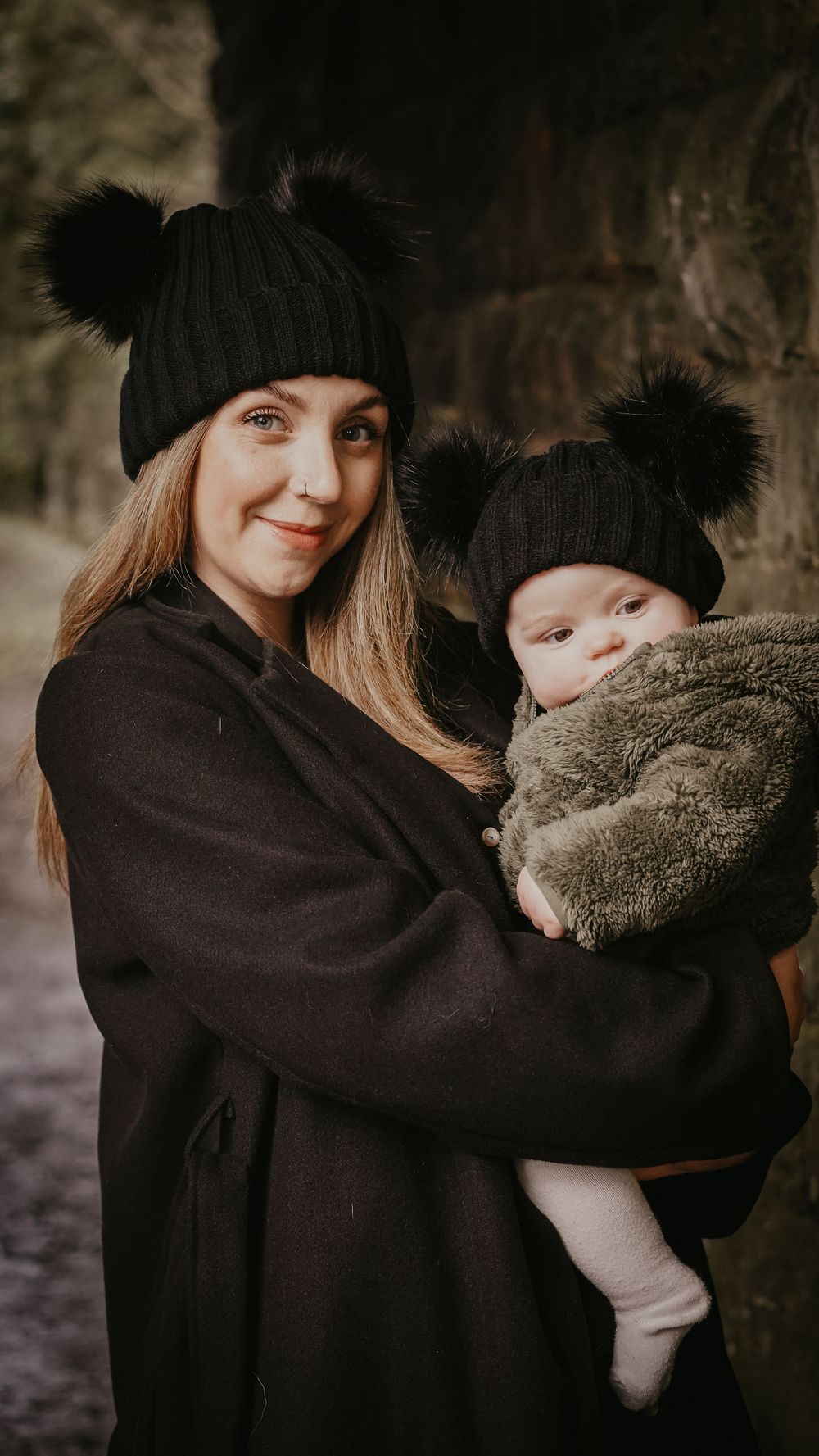 A parent in black winter clothing holds and embraces a small child wrapped in a cozy blanket.