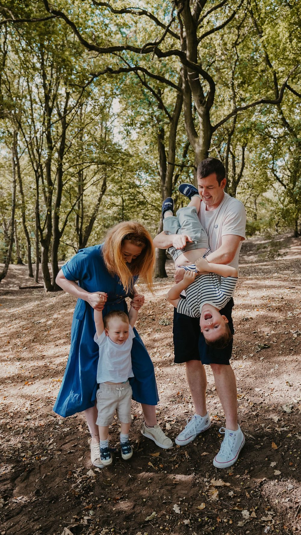 A family enjoys playful moments together while sitting on a dirt path in a forest setting.
