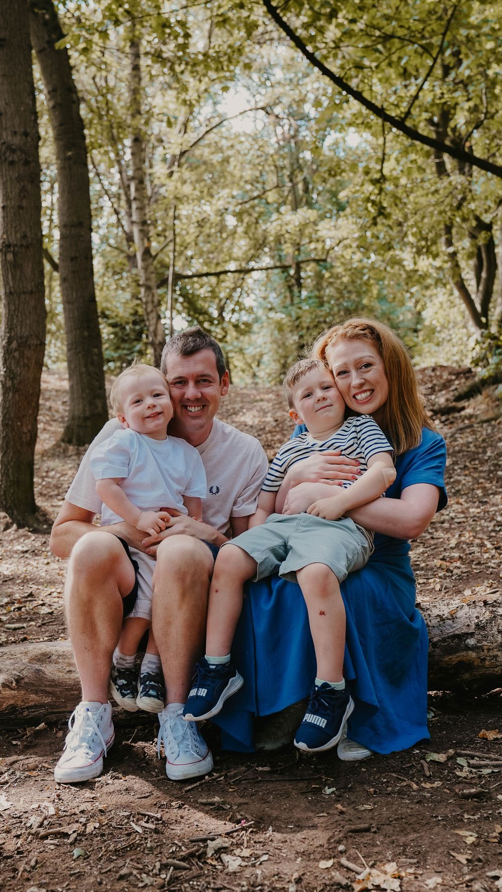 A group sits together on a log in the woods sharing laughs and embraces.