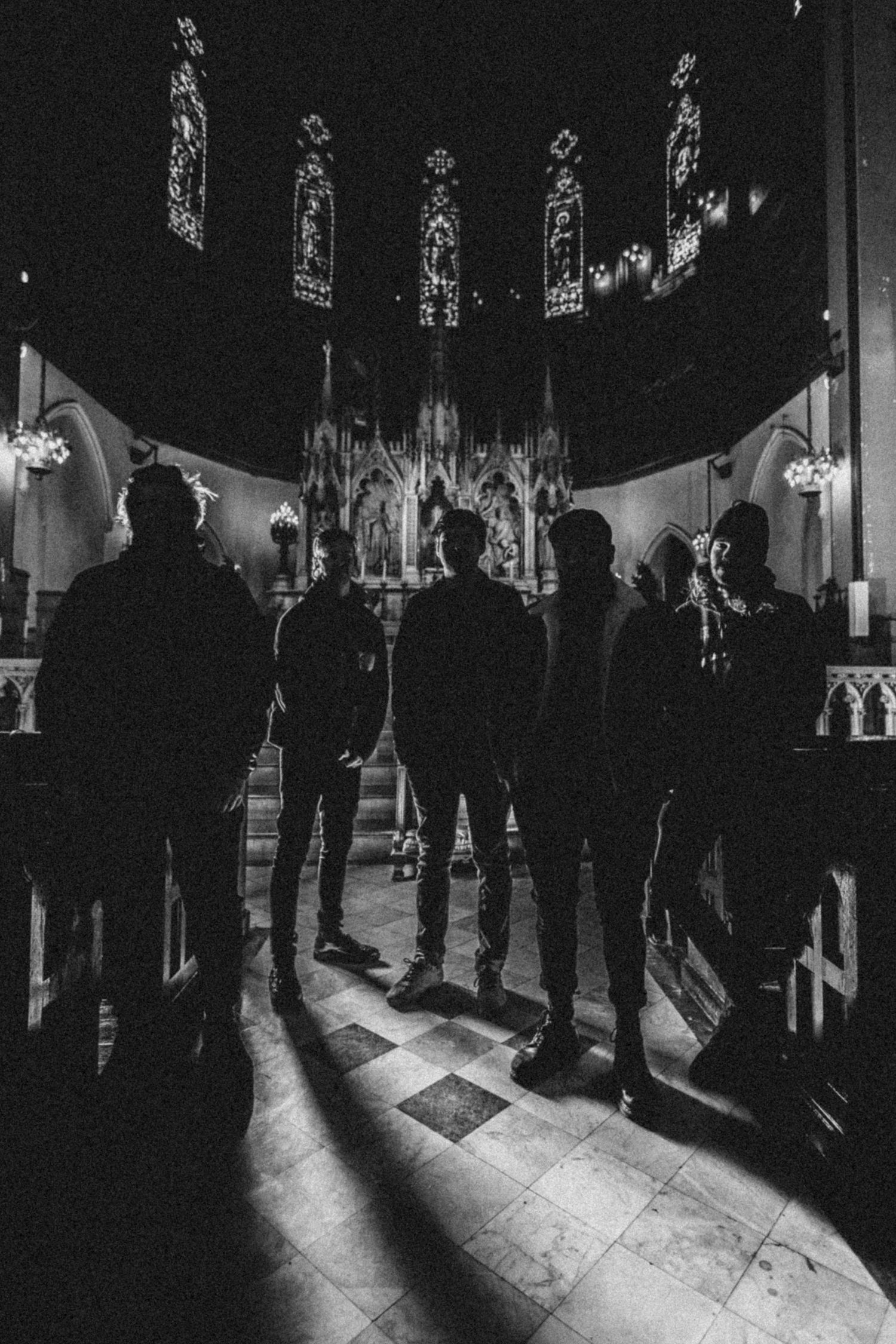 Silhouettes of five people standing in a dark Gothic church with stained glass windows and ornate altar, black and white photo.