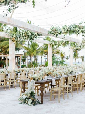 Elegant outdoor wedding reception setup with white floral arrangements and rustic wooden tables under a draped canopy.