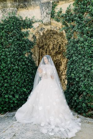 Bride in flowing white gown and veil poses in garden grotto.