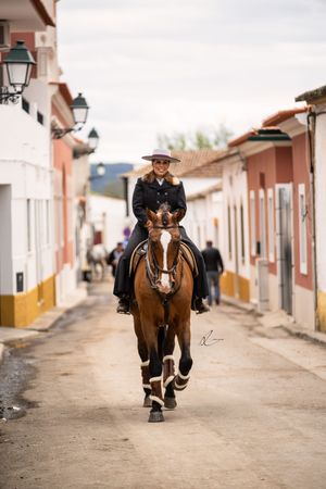 A person riding a brown horse down a narrow cobblestone street with traditional colonial architecture in the background.