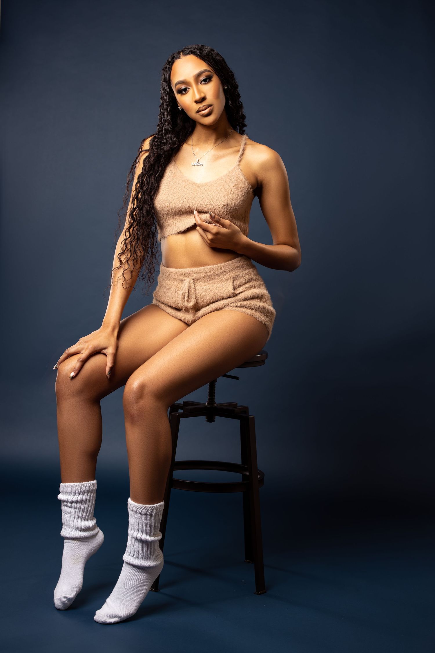Model in peach-colored loungewear set poses on a stool against dark background wearing white socks.
