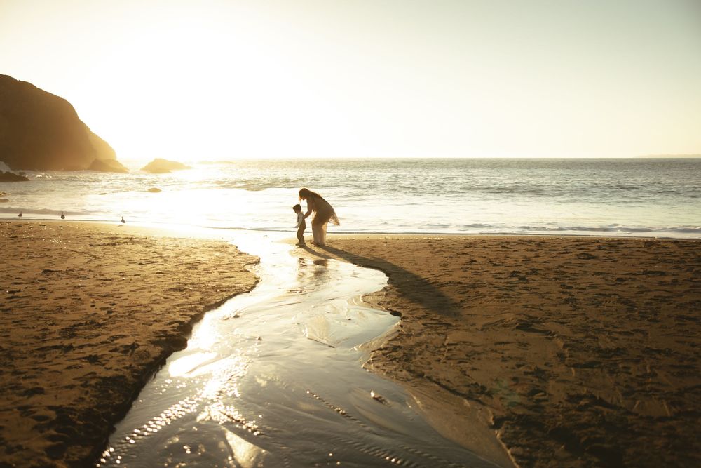 Panoramic beach scene with silhouettes playing near ocean at sunset.