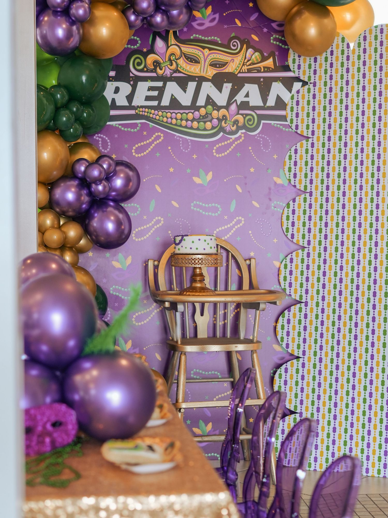 Purple and gold balloon arch with a wooden highchair setup for a first birthday party.