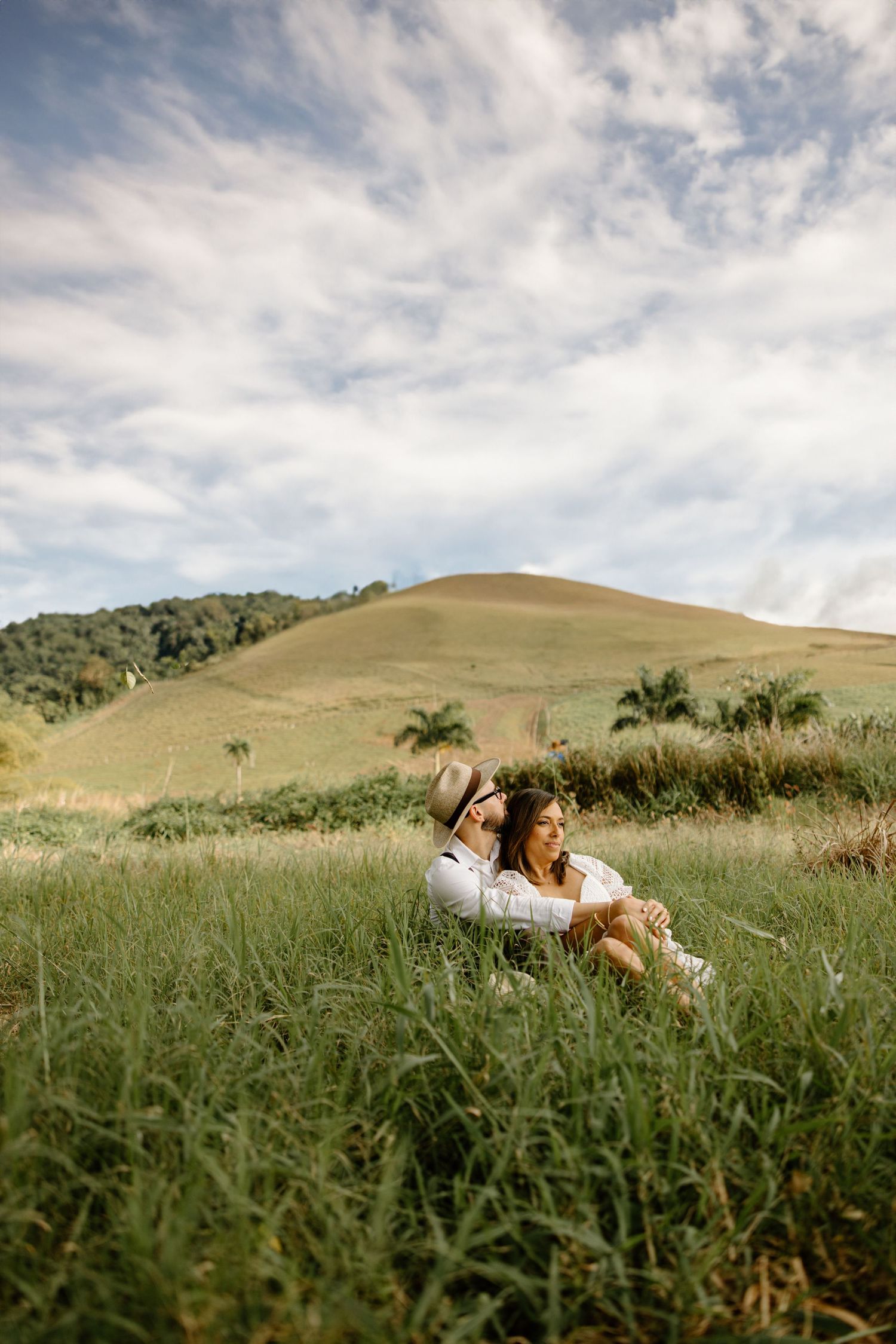 Couple relaxing in green grass field under dramatic cloudy sky.