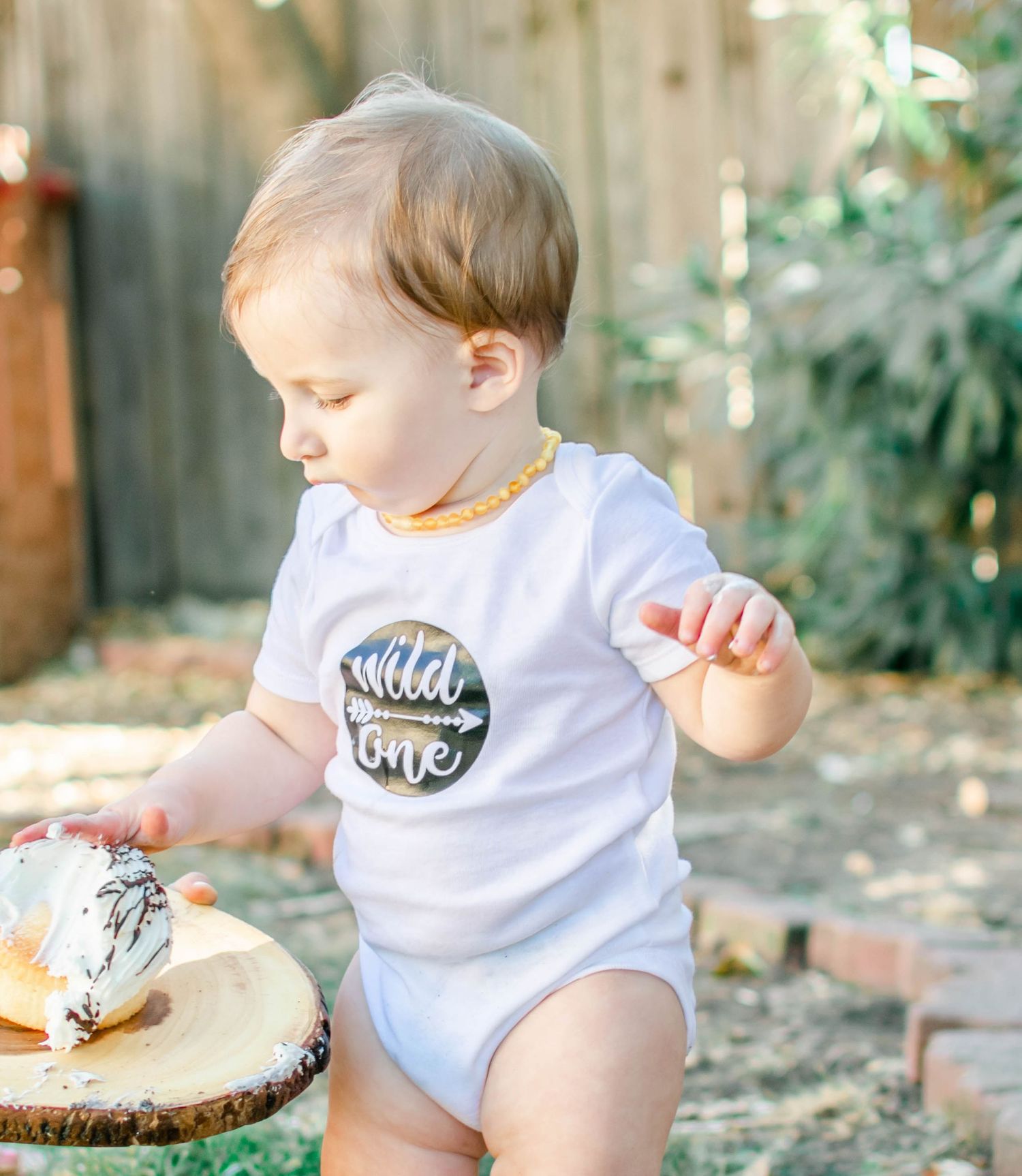 Baby in 'Wild One' outfit plays during casual outdoor photography session.