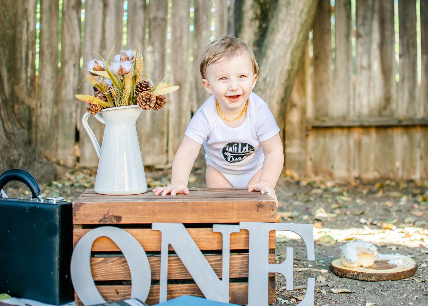 Sweet birthday cake smash photoshoot with decorative letters and rustic wooden elements in an outdoor setting.
