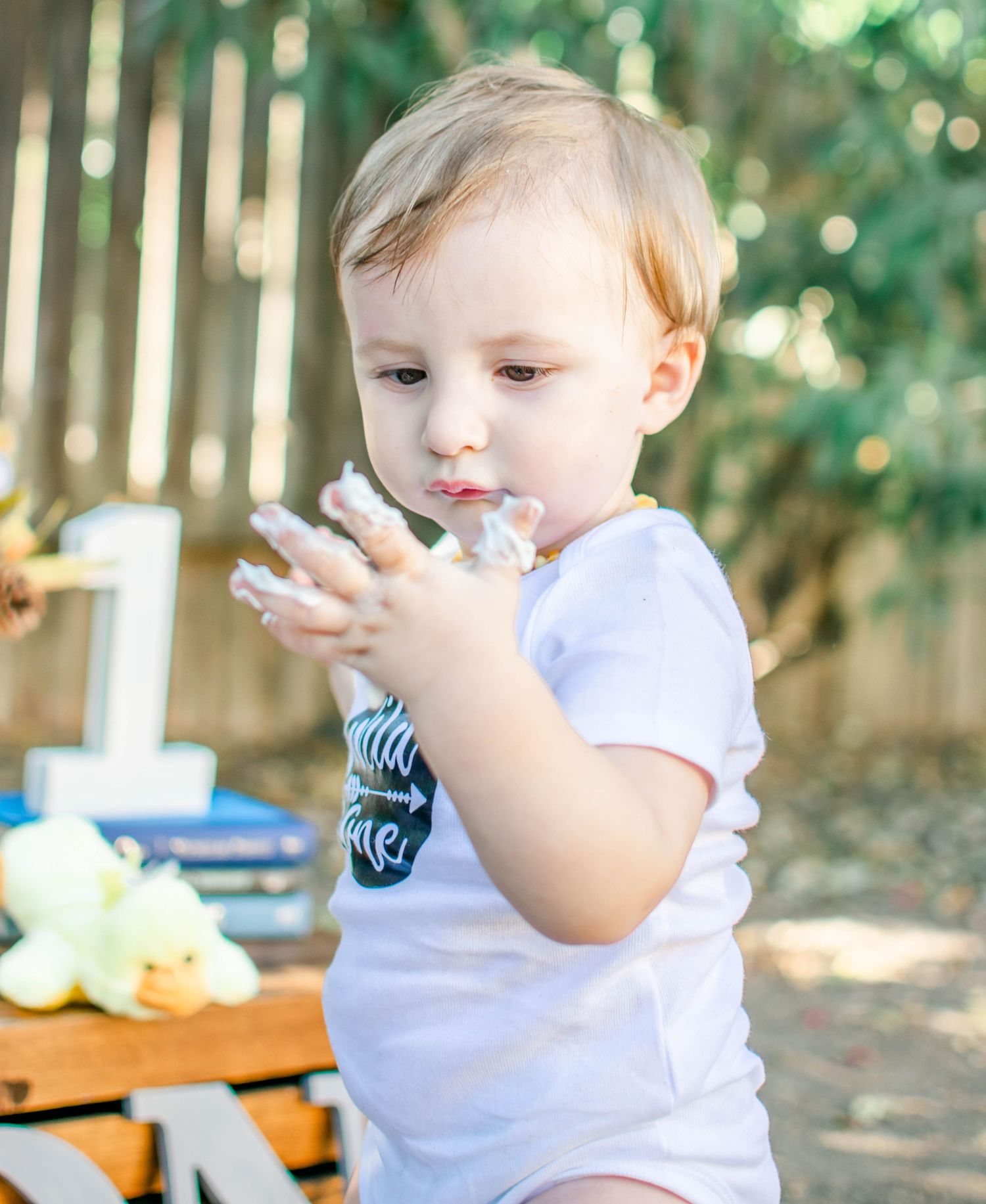 Baby tasting cake frosting during outdoor cake smash session in white onesie.