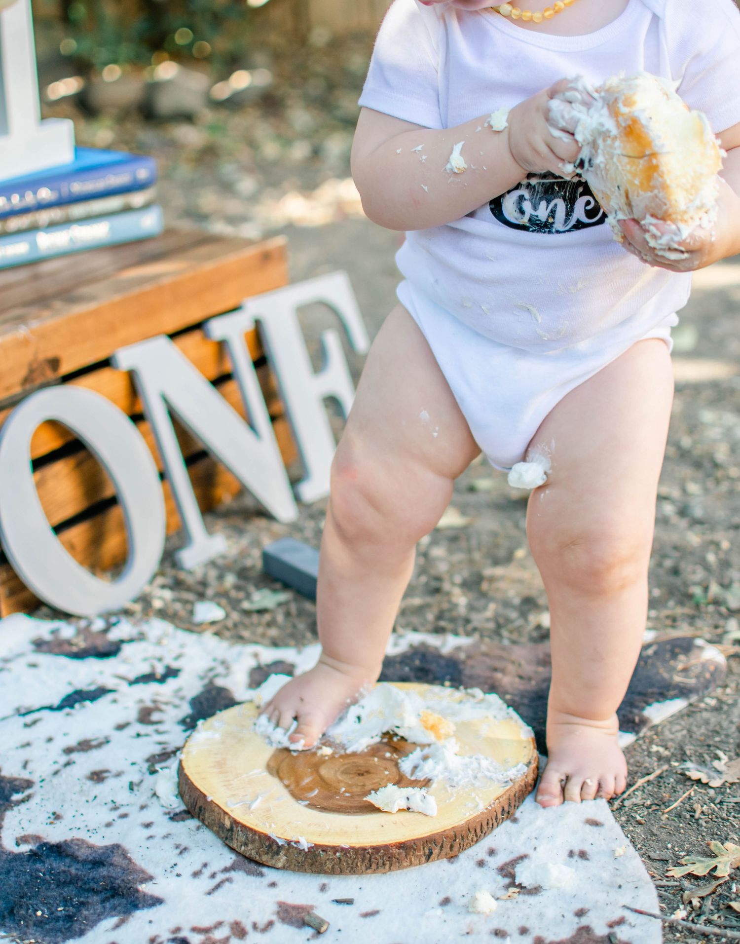 Baby's feet and hands covered in cake during outdoor first birthday celebration.