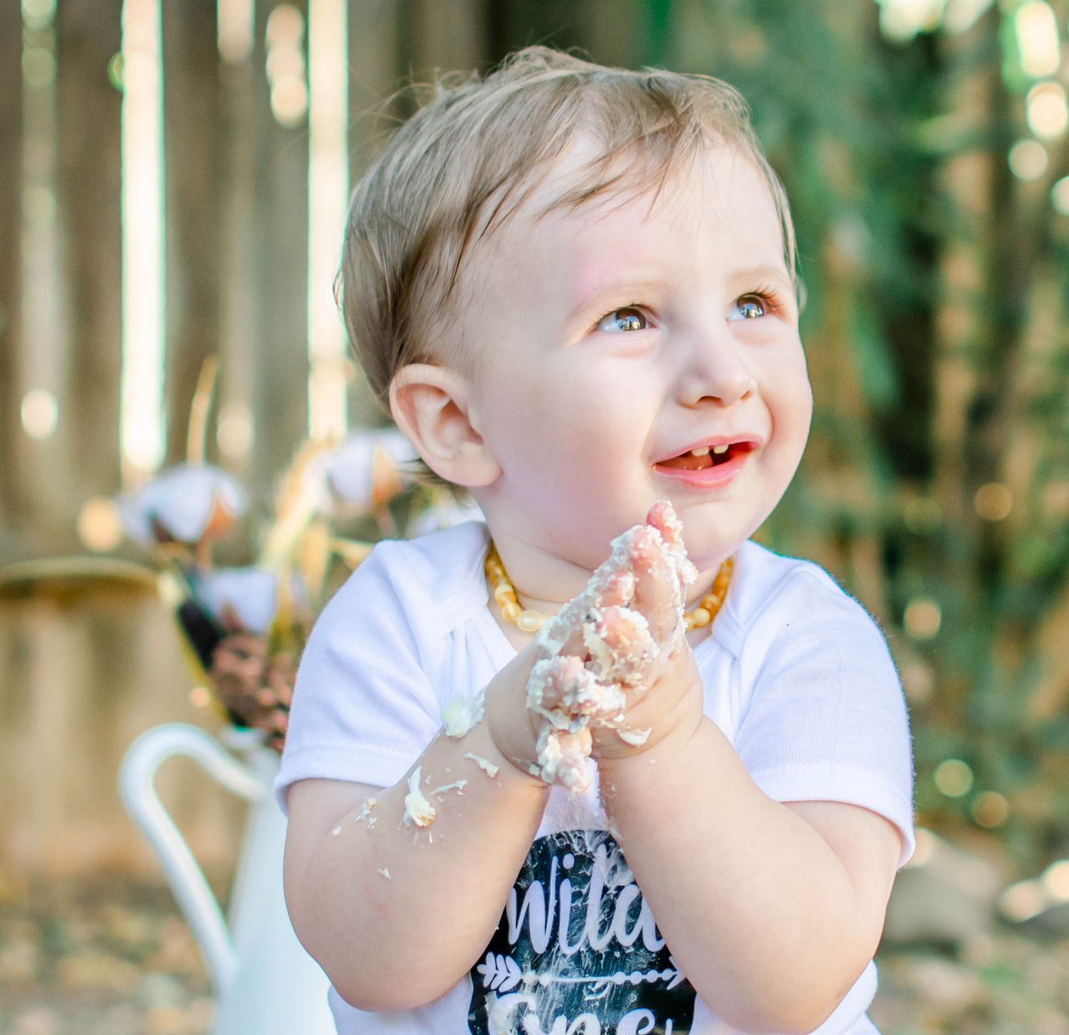 Baby enjoying cake with messy hands during outdoor first birthday photoshoot.