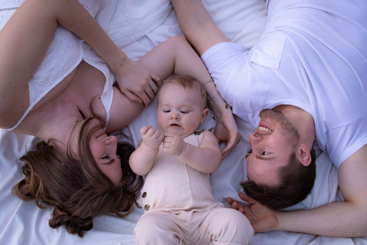 Family lying together on white bedding in a tender moment.