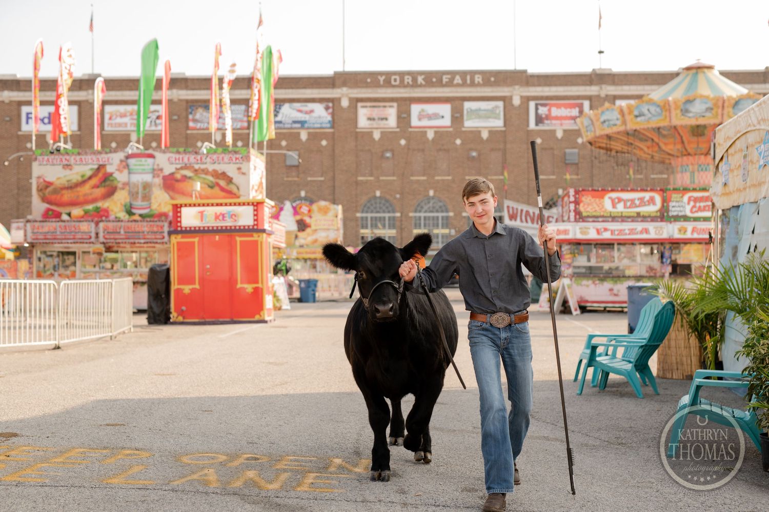 A black show cow walks with its handler along the carnival midway with festive decorations.