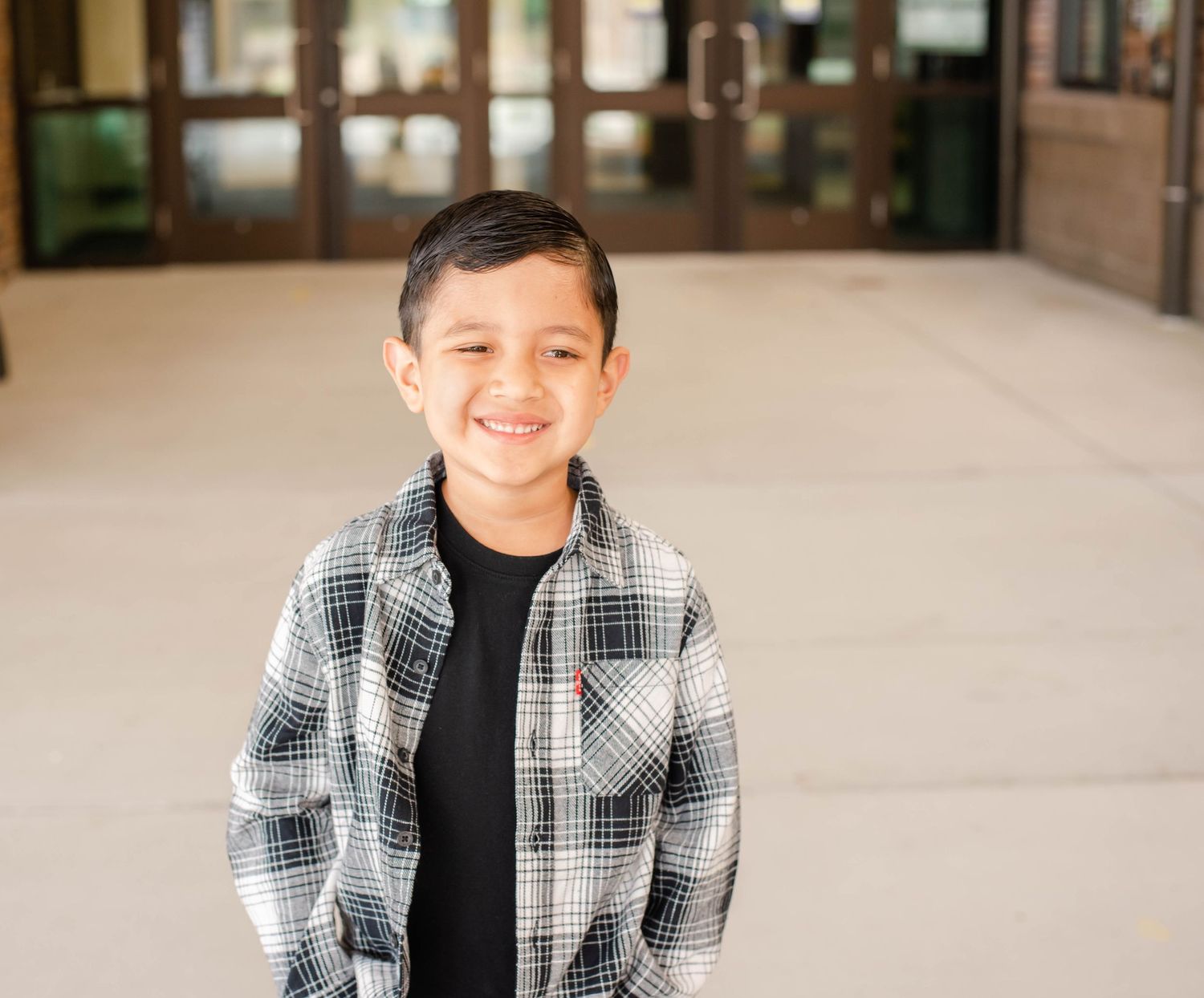 Young graduate in plaid shirt smiles at camera in indoor setting.