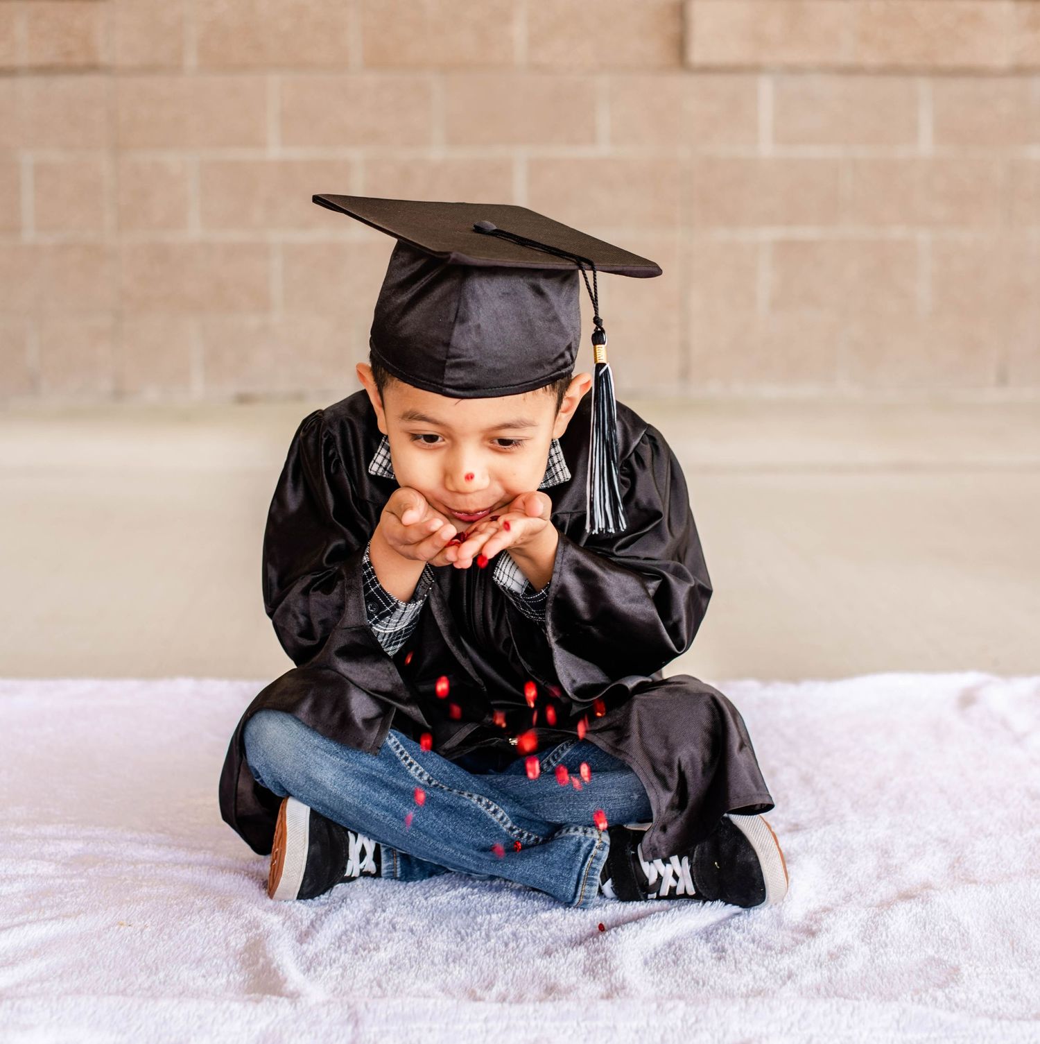 Playful graduation photo session with confetti and black academic regalia.