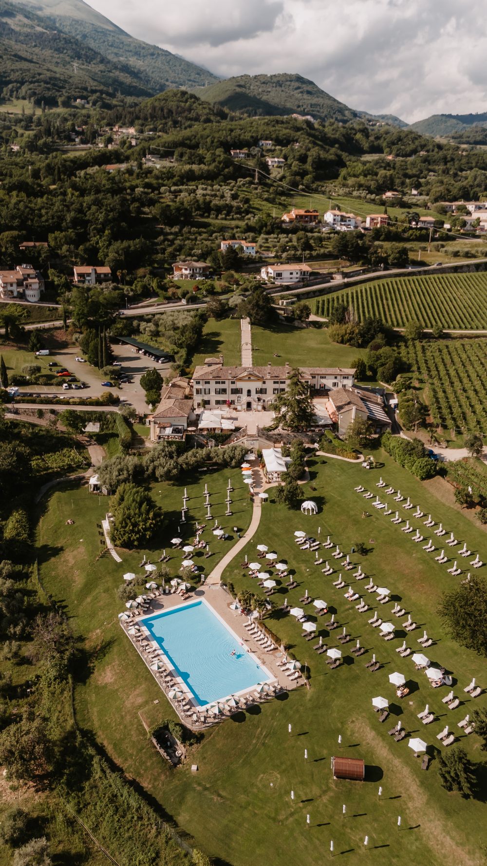 Aerial view of a luxury resort with swimming pool and loungers nestled in mountainous countryside.