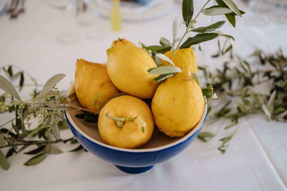 Fresh yellow lemons arranged in a blue and white porcelain bowl with olive branch garnish.