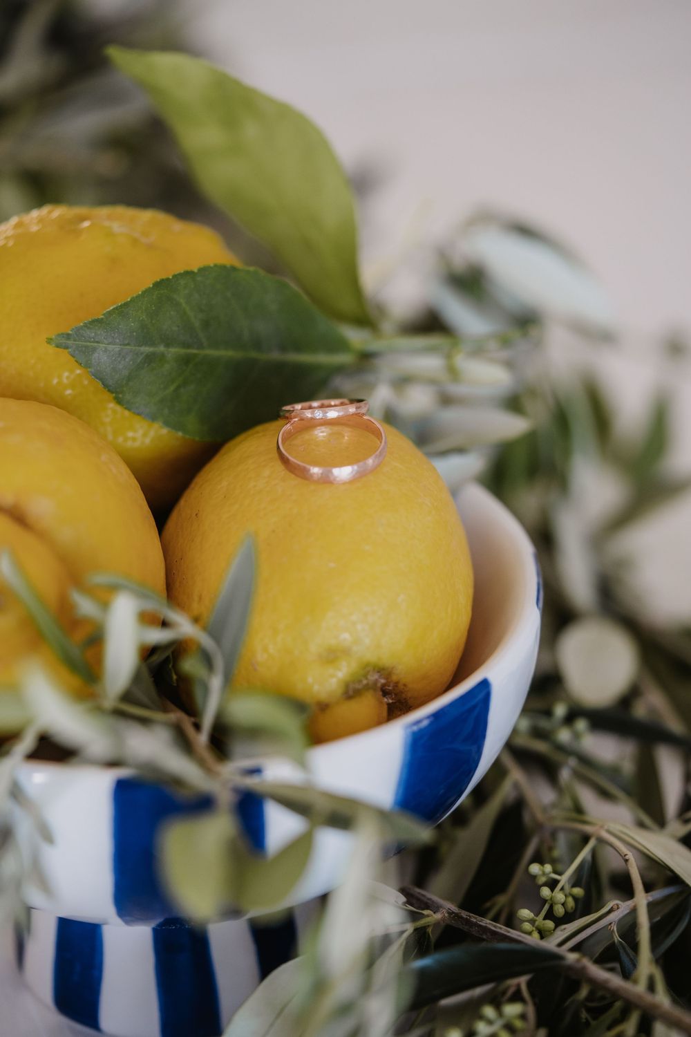 Wedding rings displayed on bright yellow lemons in a striped blue and white bowl.