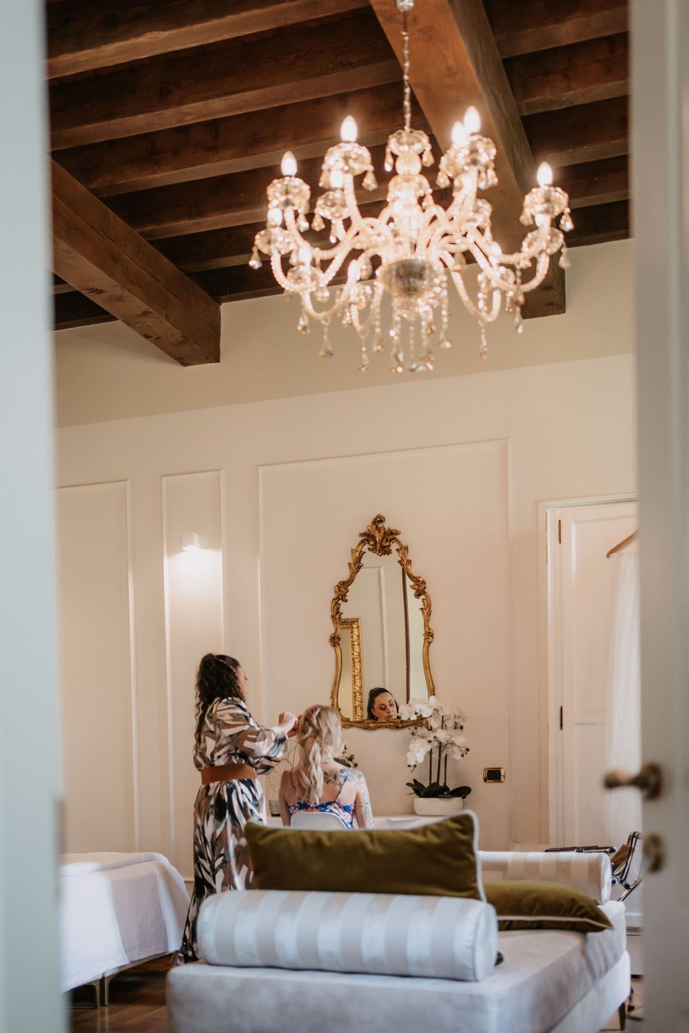 Luxurious bridal suite with crystal chandelier and ornate gold mirror under exposed wooden beams.