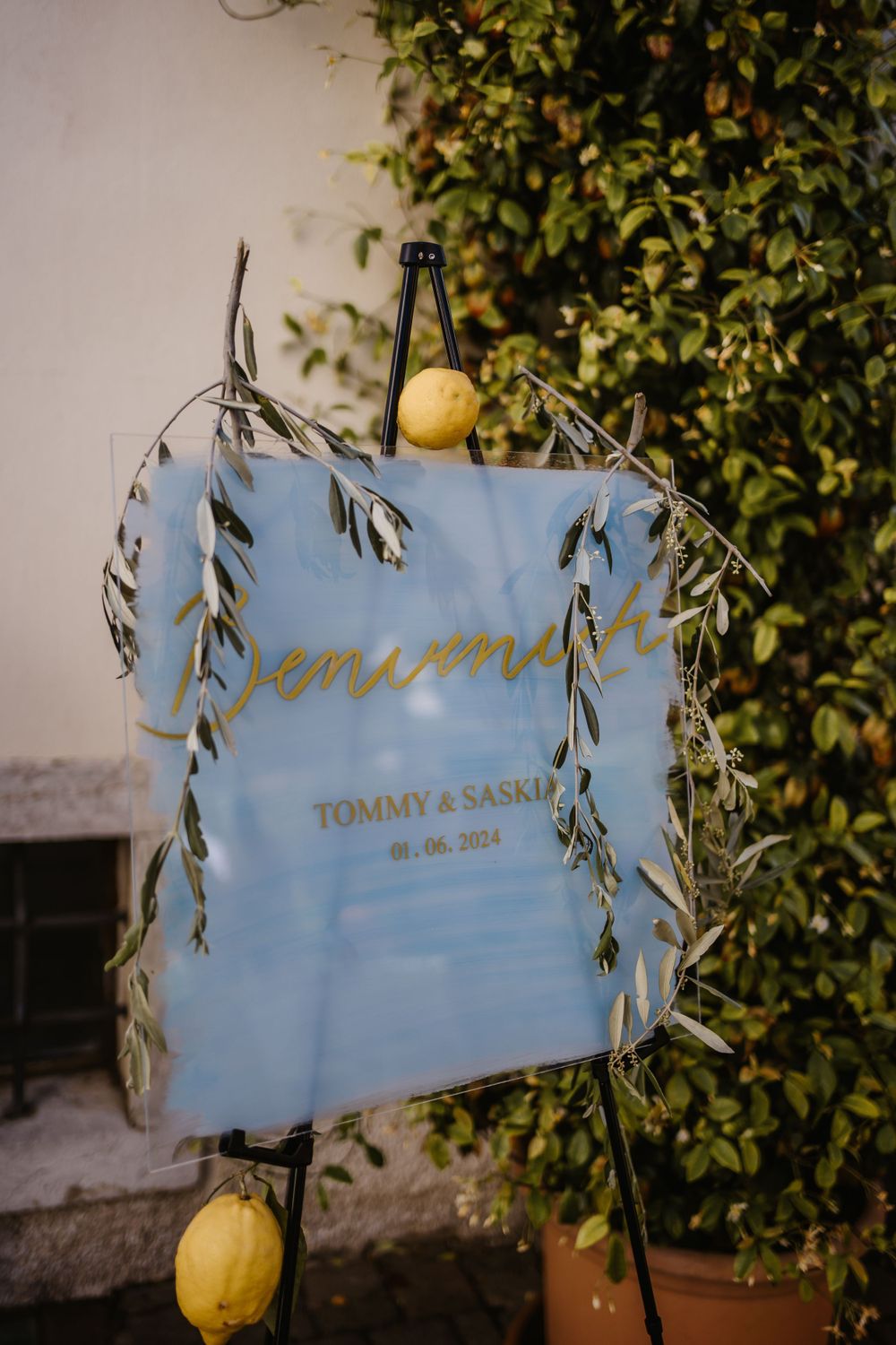 Wedding sign decorated with lemons and greenery displaying 'Tommy & Sarah' against a white wall.