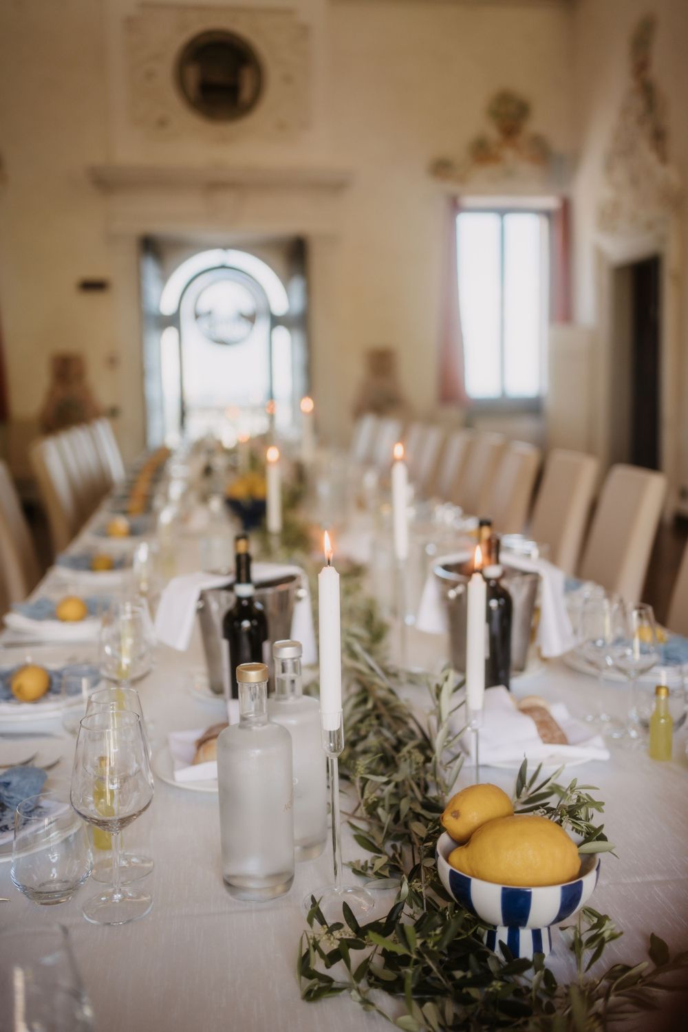 Elegant wedding table setting with white linens, candlesticks, wine bottles, and fresh lemons in blue striped bowls.