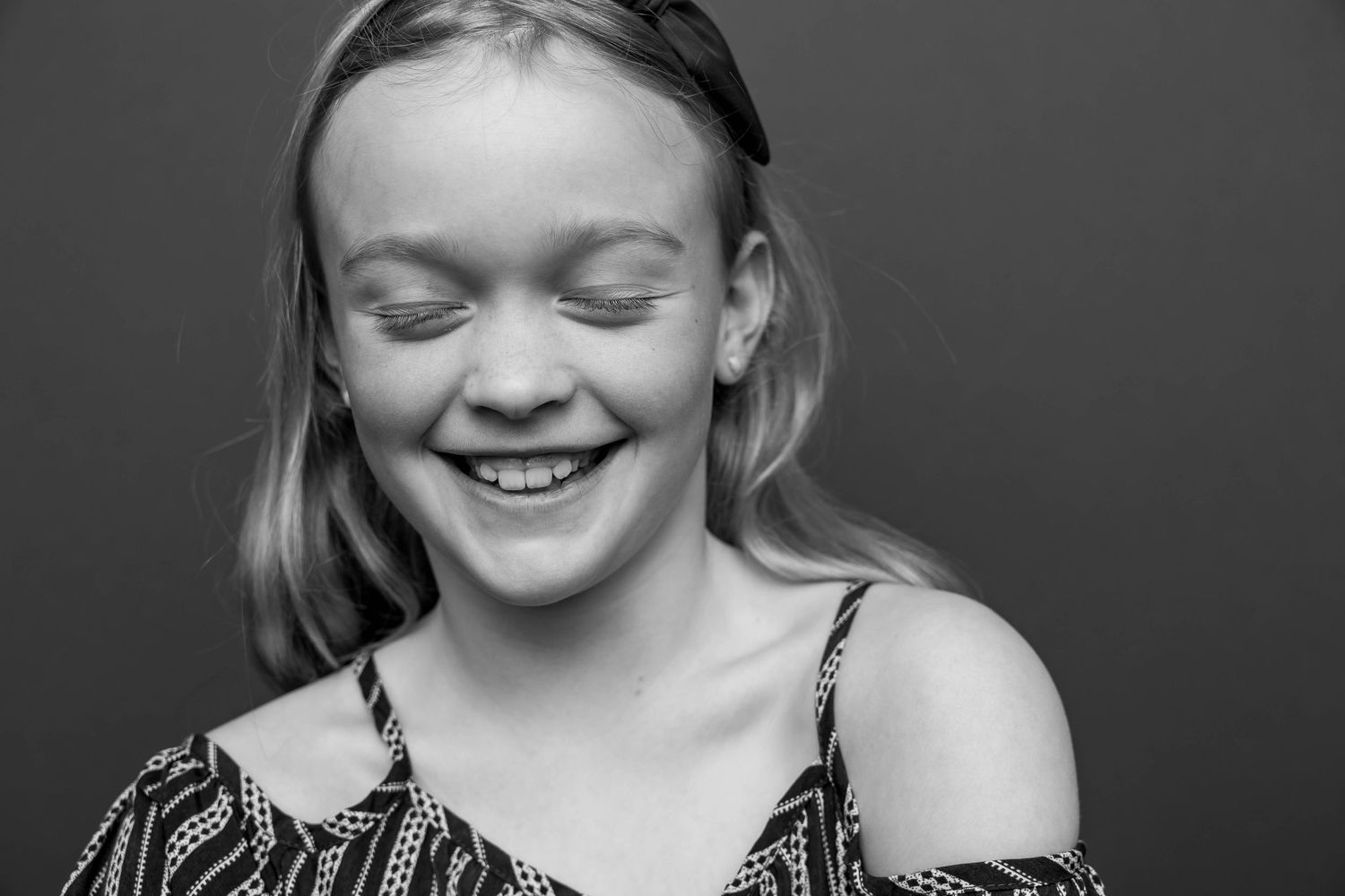 Black and white portrait of a person with closed eyes and bright smile.