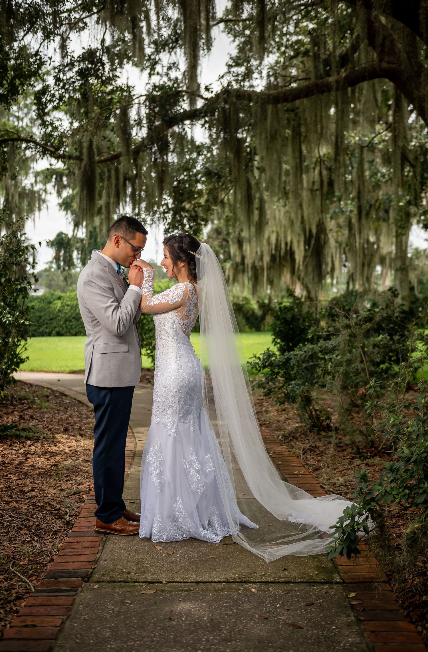 A couple shares a romantic moment under Spanish moss draped trees on a brick pathway.