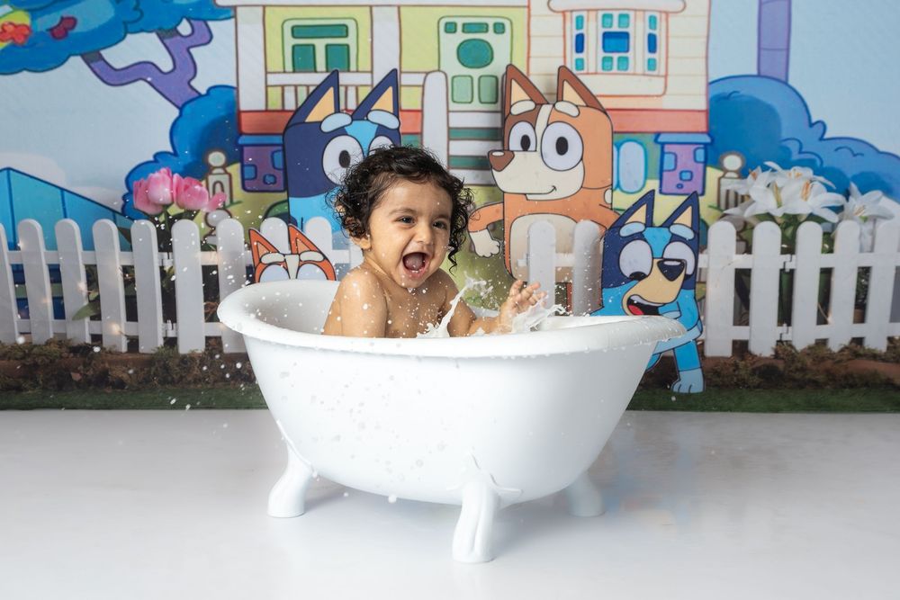 Cake smash photography setup with white bathtub against cartoon-style backdrop with houses.