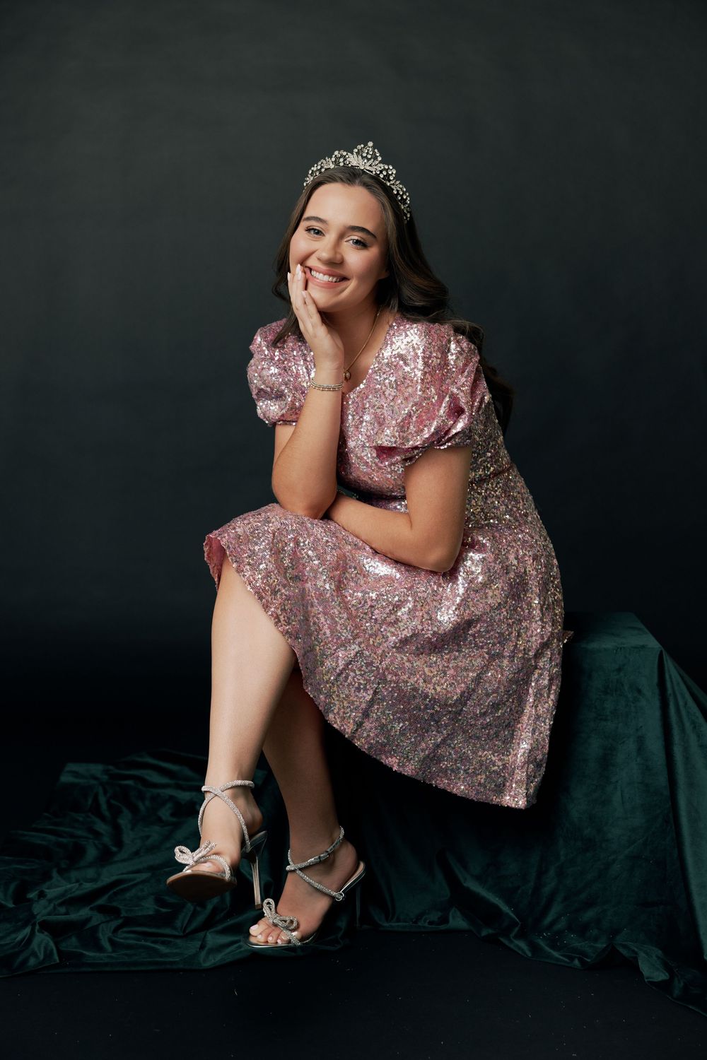 A sparkly pink sequined dress and silver heels are showcased against a dark backdrop in a glamorous portrait session.
