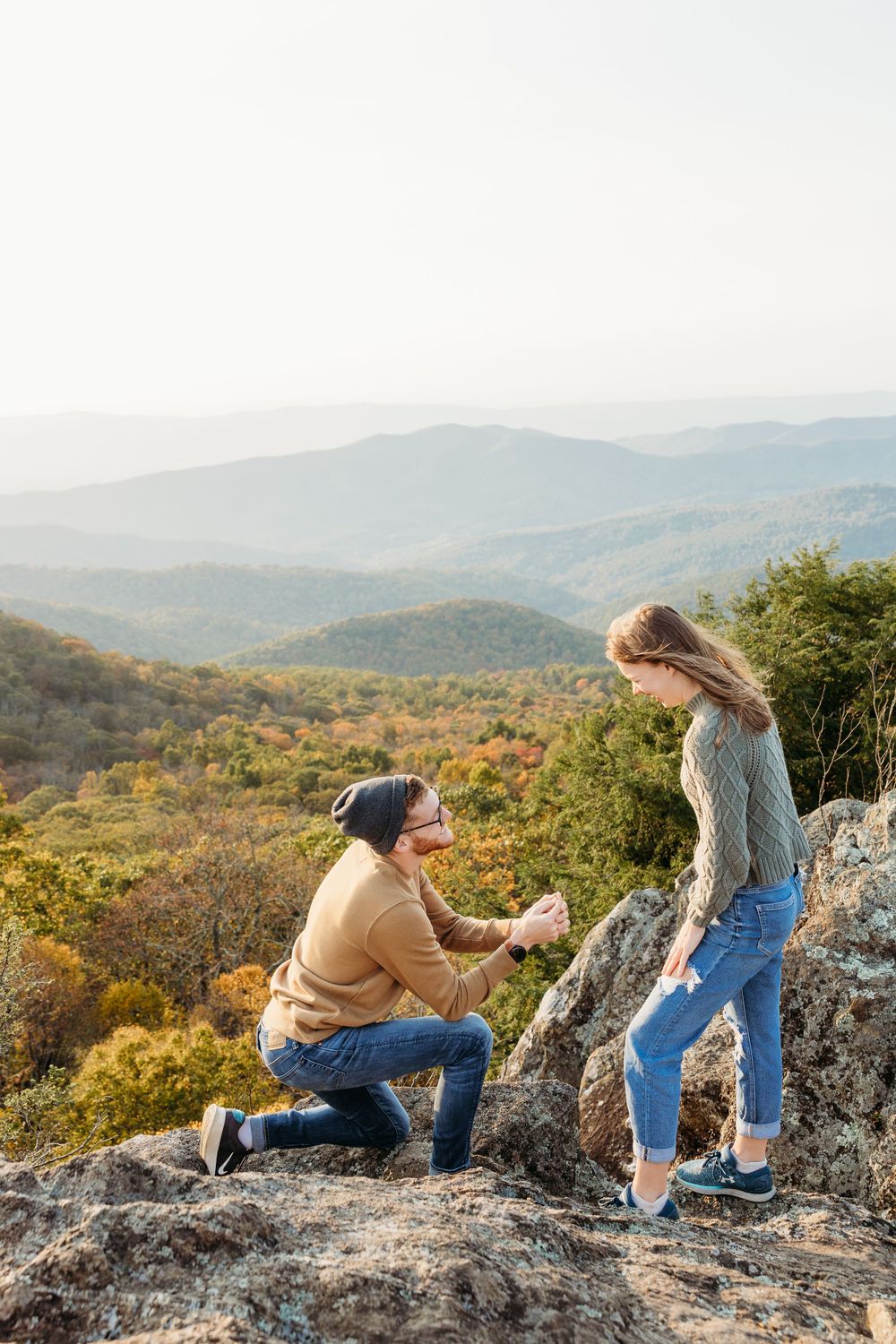 A romantic proposal scene on a scenic mountain overlook during autumn with mountains and forests in the background.