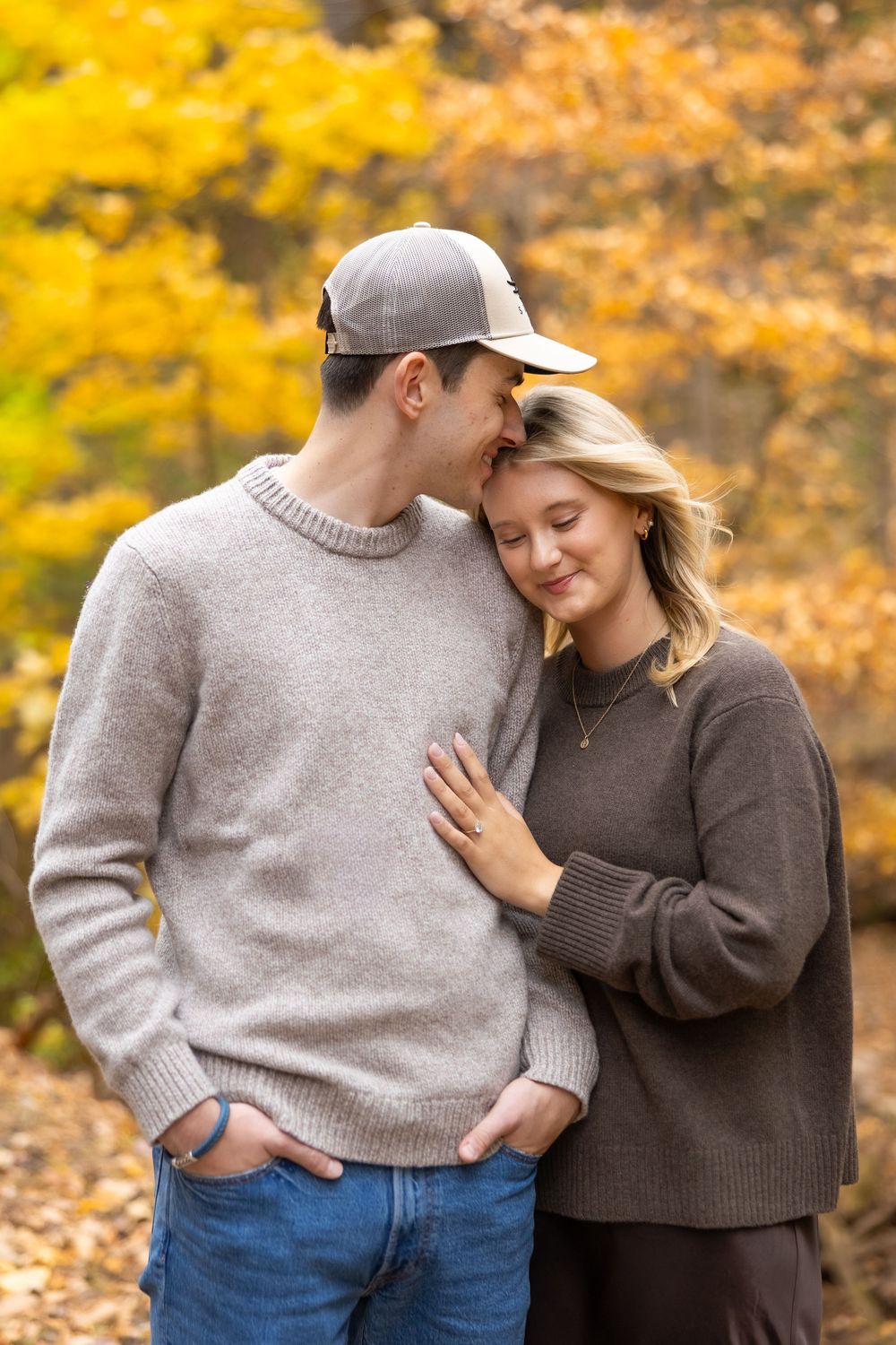 A couple shares tender moments in a park during autumn with golden yellow foliage in the background.