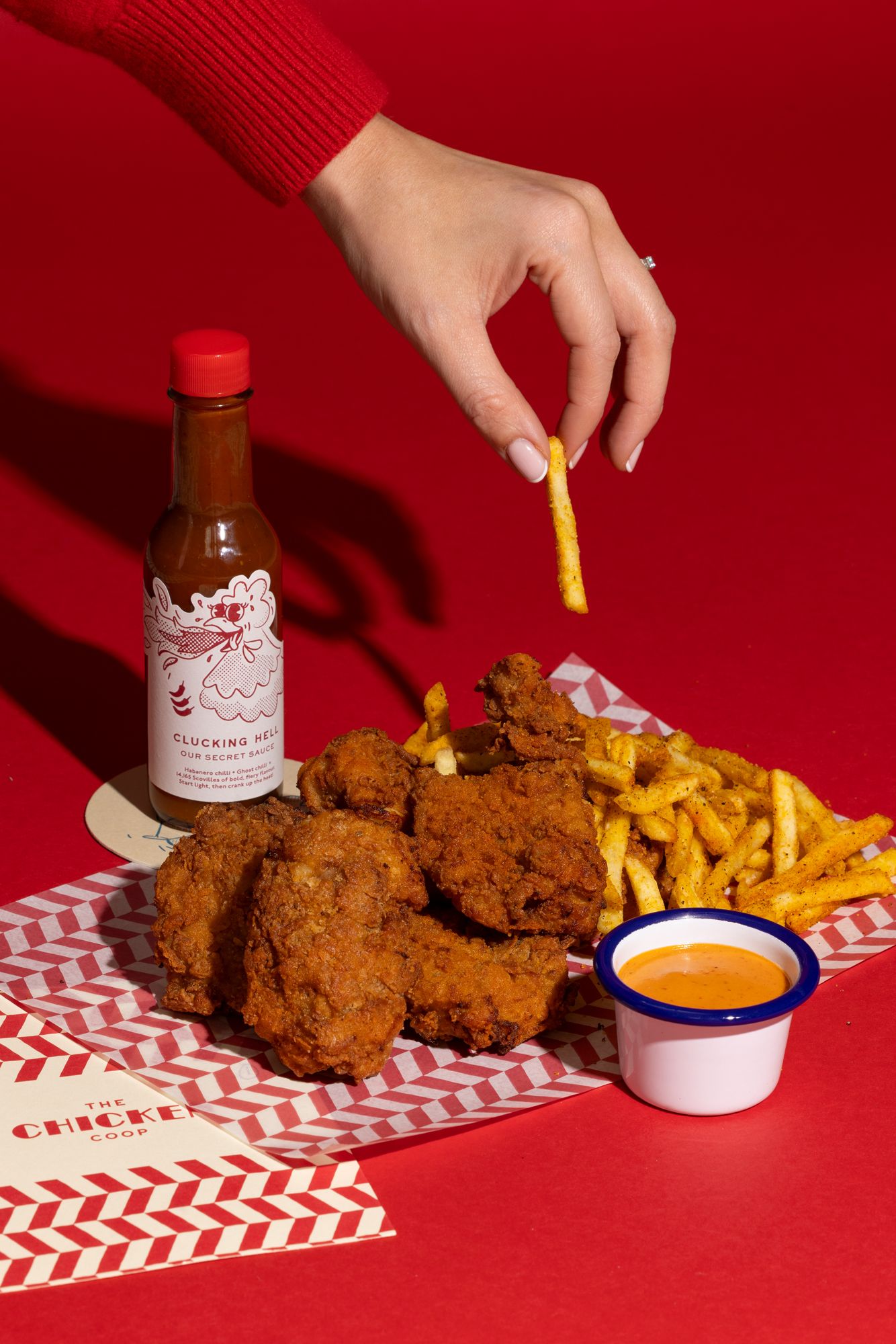 Crispy fried chicken and french fries served on red and white chevron paper with dipping sauce and condiments.