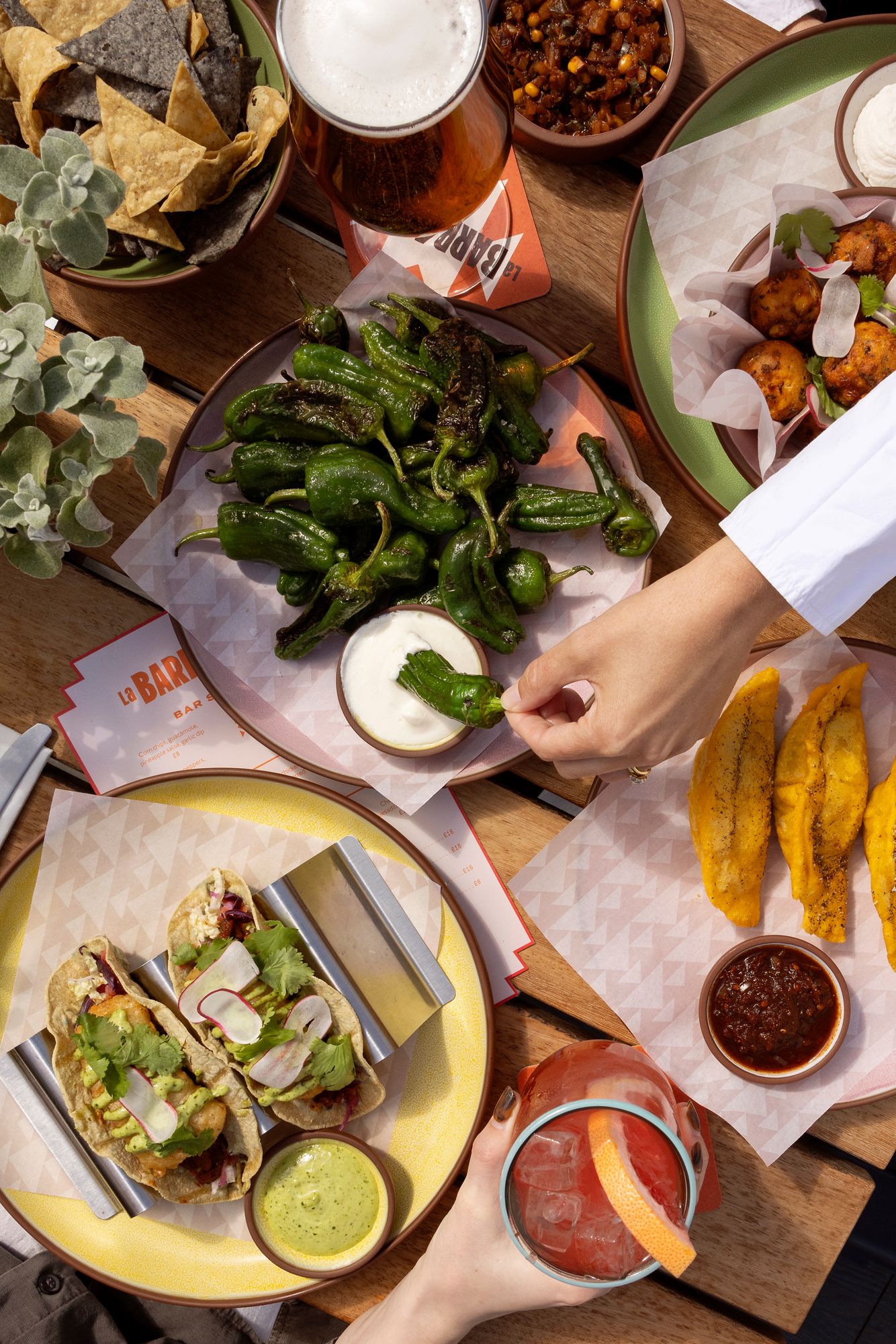 Mexican restaurant table spread with tacos, dips, sauces and appetizers on a rustic wooden surface.