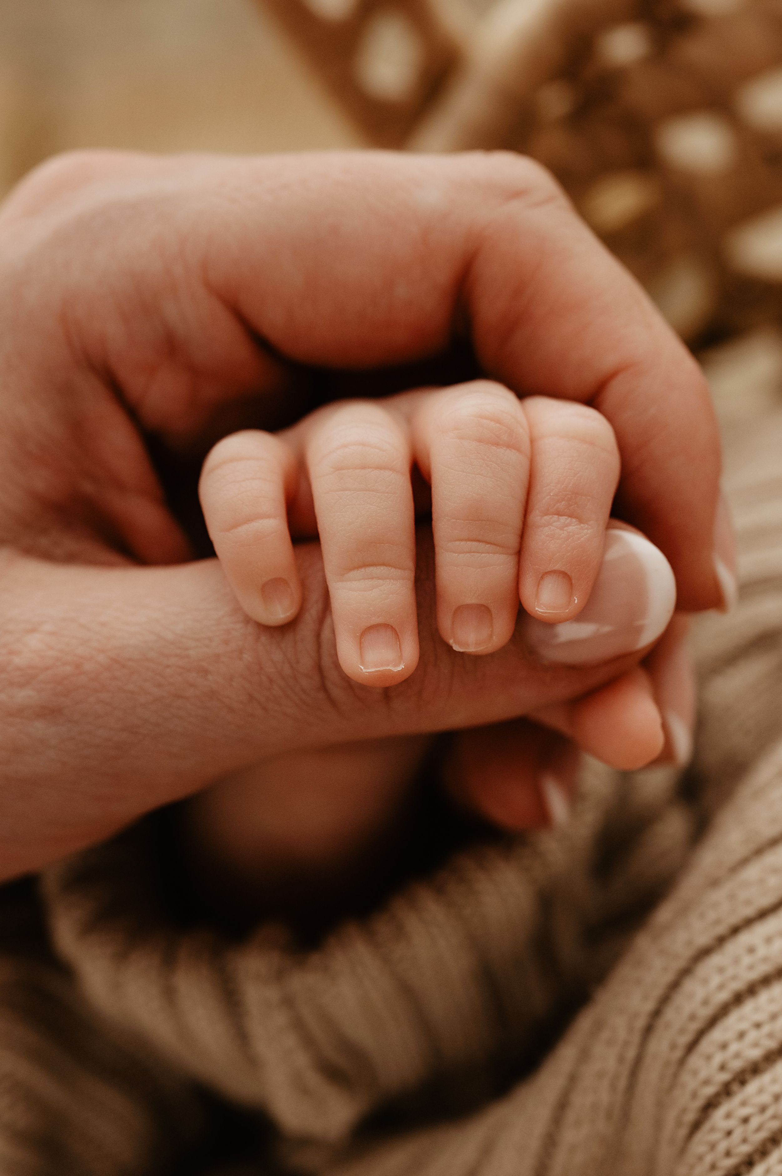 Close-up of tiny baby hand holding adult finger against knit fabric background.