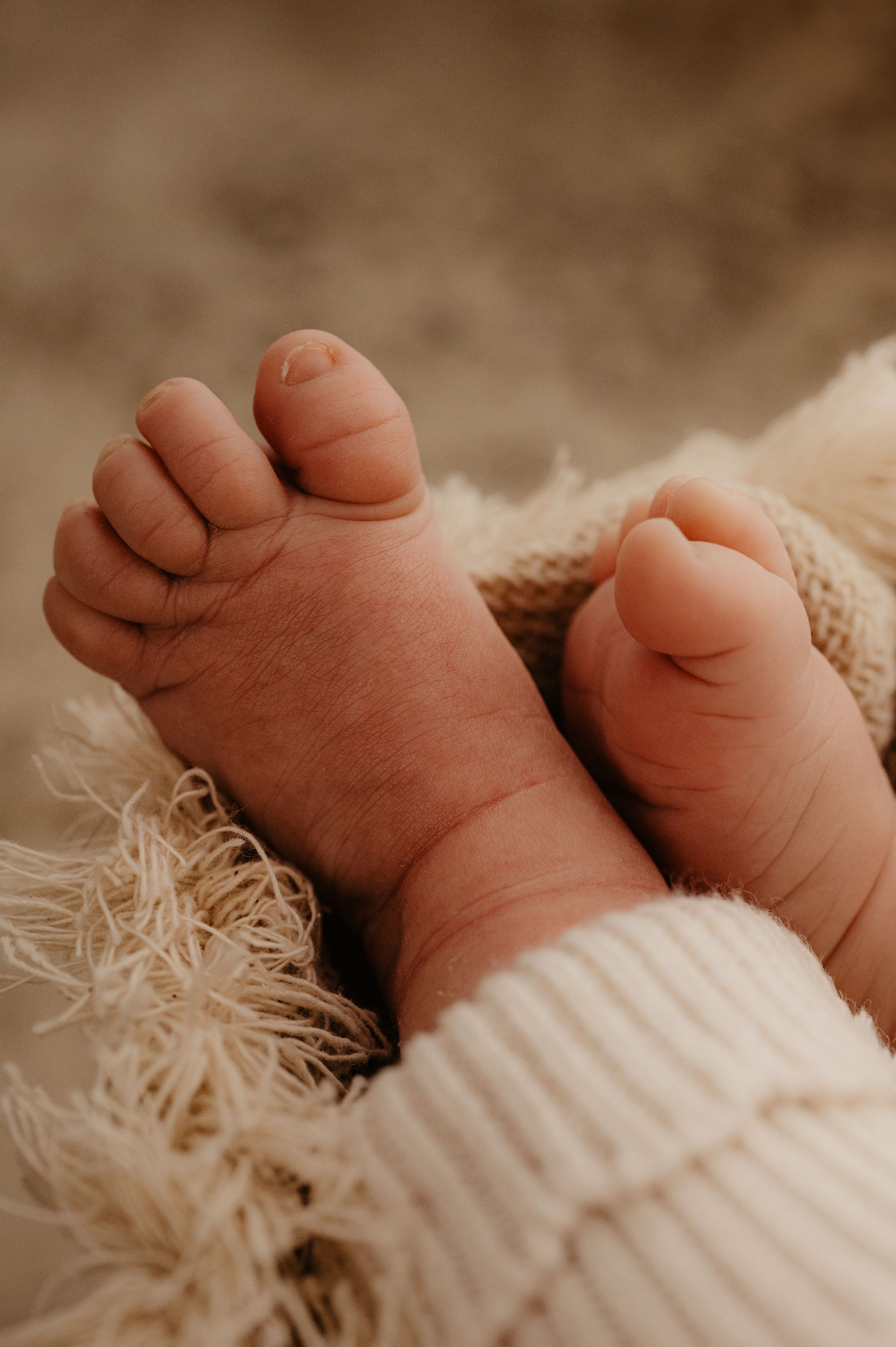 Close up detail of tiny newborn baby toes against soft white knit fabric in warm lighting.