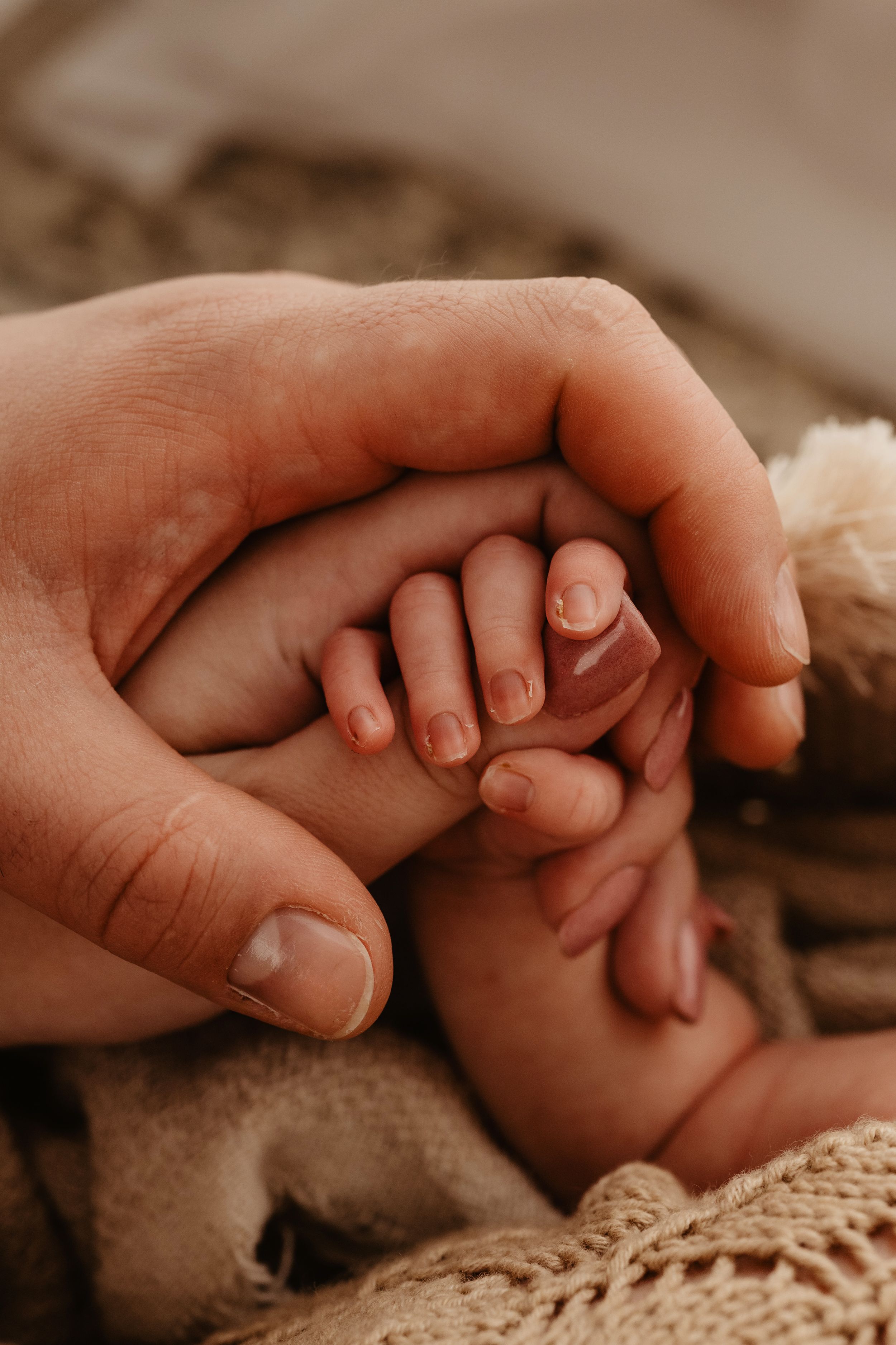 Two hands gently clasped together against a soft knitted fabric background in warm lighting.